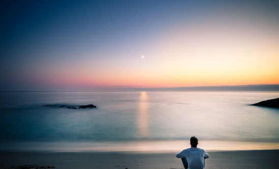Man Sitting On Sandy Beach During Sunset